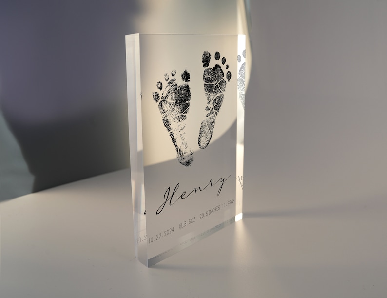 Op de afbeelding: Helder acrylblok met zwarte inkt baby-voetafdrukken en de naam "Henry" samen met de datum "10.22.2024", het gewicht "8,8 oz" en de lengte "20,5 inch".
