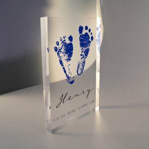 Op de afbeelding: Een transparante acrylblok met blauwe baby-voetafdrukken en de naam "Henry" gegraveerd. De datum "10.22.2024" en het gewicht en de lengte van de baby zijn ook opgenomen.