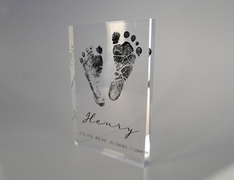 Op de afbeelding: Een heldere acrylblok met een zwarte inktindruk van babyvoetjes. De blok bevat ook de naam "Henry", de datum "10.22.2024", het gewicht "8.8 LB 6OZ", de lengte "20.5 INCHES" en de tijd "11:28AM".