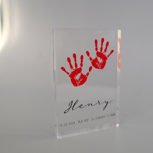 Op de afbeelding: Een transparante acrylblok met twee rode handafdrukken en de tekst "Henry 10.10.2024 8LB 6OZ 20.5 INCHES 11:28AM"