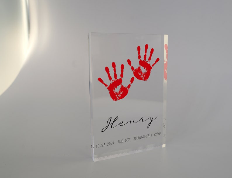 Op de afbeelding: Een transparante acrylblok met twee rode handafdrukken en de tekst "Henry 10.10.2024 8LB 6OZ 20.5 INCHES 11:28AM"