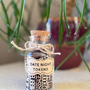 K&ouml;nnte beinhalten: Ein kleines Glas mit einem Korken und einer Schnur-Schleife, gef&uuml;llt mit Holzmarken. Auf dem Etikett steht "DATE NIGHT TOKENS". Die Marken tragen W&ouml;rter wie "HUG", "CUDDLE" und "MASSAGE".