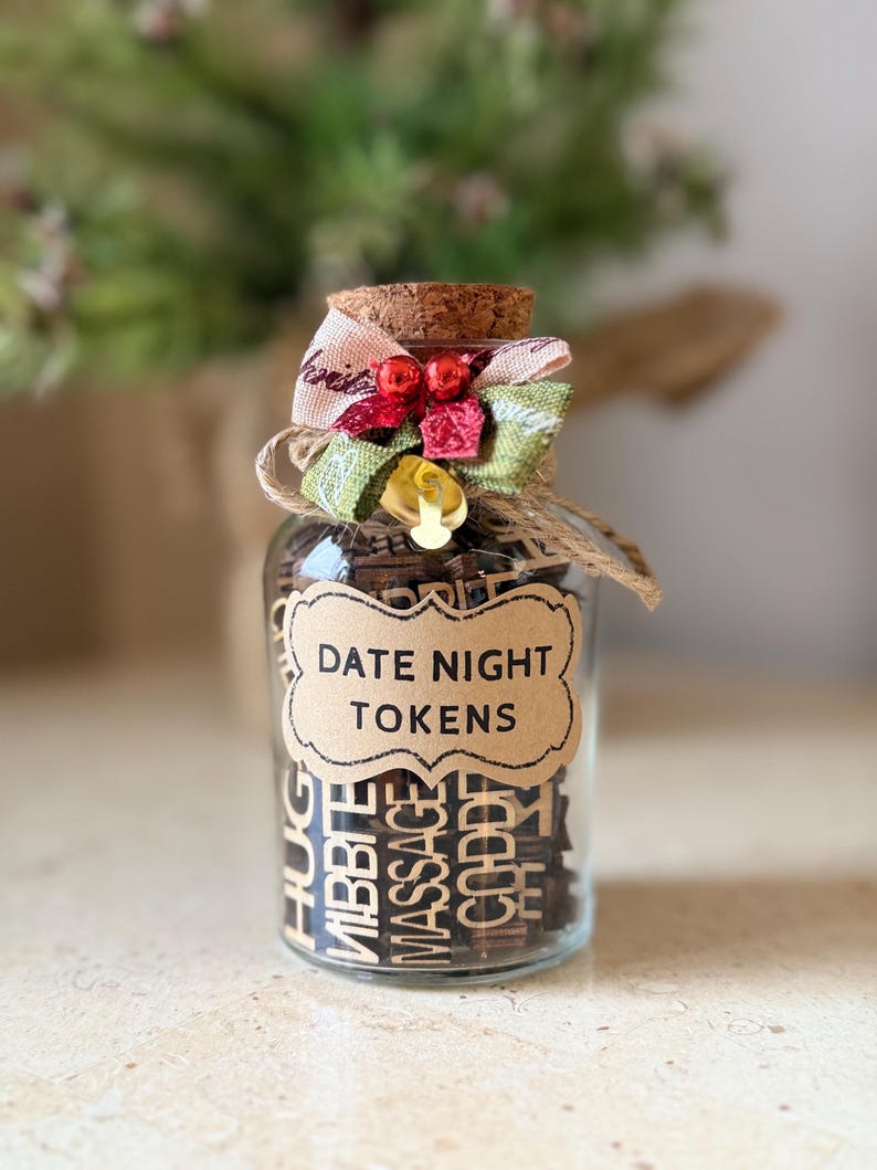 K&ouml;nnte beinhalten: Ein klares Glas mit Holzmarken, beschriftet mit "DATE NIGHT TOKENS". Das Glas ist mit einem Korken, einer dekorativen Schleife und Bindfaden verziert. Die Marken enthalten verschiedene romantische Aktivit&auml;tsvorschl&auml;ge.