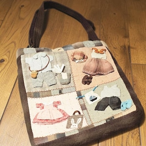 May include: A brown fabric shoulder bag featuring a patchwork design with appliquéd miniature clothing items, including dresses, shirts, trousers, hats, and a small bag with a rabbit face, all rendered in various muted textile patterns and colours.
