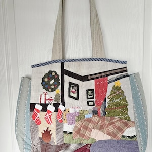 May include: A quilted tote bag featuring a festive holiday interior scene with a fireplace, three hanging stockings, a decorated Christmas tree, wrapped gifts, and a wreath. The bag has light beige handles and light blue side panels.