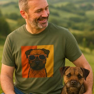 May include: Olive green t-shirt with a graphic of a dog wearing sunglasses. The dog is brown with black accents, set against a yellow and orange background. A real dog of the same breed is next to the person wearing the shirt.