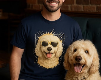 Könnte beinhalten: Ein marineblaues T-Shirt mit einer Cartoon-Illustration eines Golden Retrievers mit Sonnenbrille. Ein echter Golden Retriever-Hund sitzt neben der Person, die das Shirt trägt. Der Hintergrund umfasst eine Backsteinmauer und ein dunkelgrünes Sofa.