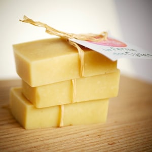 Peut inclure: Un empilement de quatre barres de savon rectangulaires liées avec de la ficelle et une étiquette qui indique "La Ferme des Cygnes".