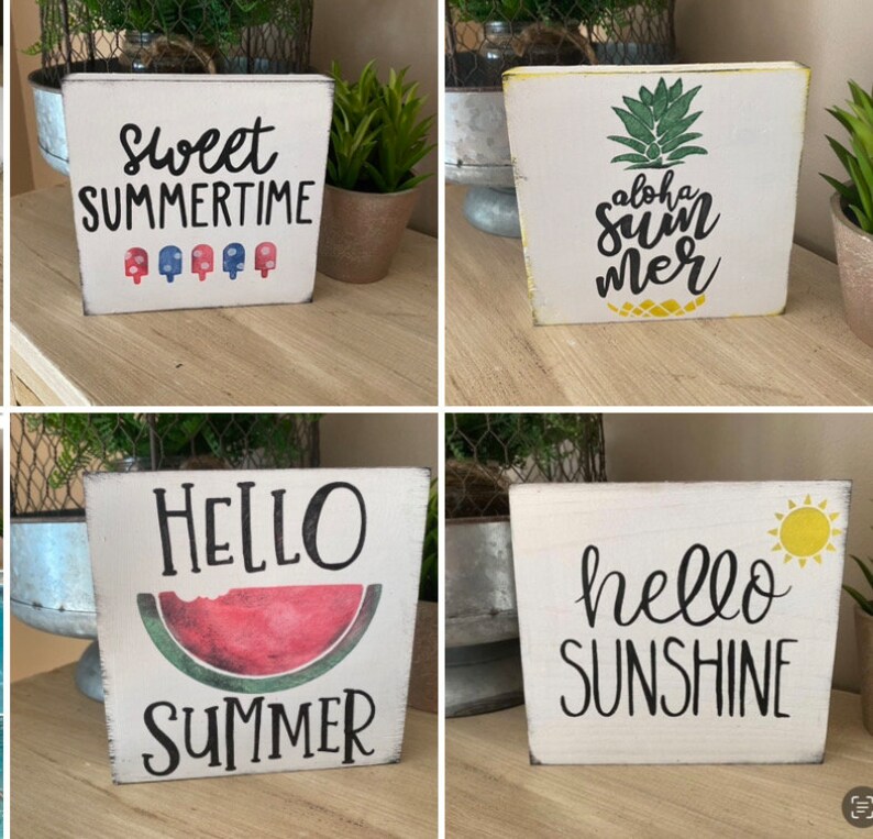 May include: Four white wooden blocks with summer designs. One block says "Sweet Summertime" with popsicle graphics. Another has a pineapple and "Aloha Summer" text. A third says "Hello Summer" with a watermelon. The last says "Hello Sunshine" with a sun.