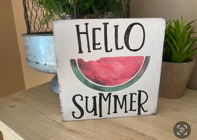 May include: A square, white wooden sign with the words "HELLO SUMMER" in black script. A watercolor-style watermelon slice is in the center. The sign has a distressed, rustic look, ideal for summer decor.