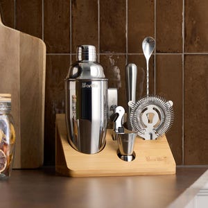 May include: A stainless steel cocktail shaker set with a bamboo stand. The set includes a shaker, strainer, jigger, spoon, and muddler. The brand name "Barillo" is visible on the shaker and jigger.