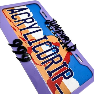 Puede incluir: Un marco de matrícula morado con un diseño de mapa colorido y las palabras "ACRYLICORP" en letras azules grandes. Las palabras "JUICEWRLD" están en negro, con tres símbolos negros "999".