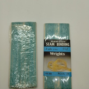 Könnte beinhalten: Zwei Rollen aquafarbener Flexi-Lace-Nahtband. Eine Rolle ist in Kunststoff verpackt. Die andere Rolle hat ein schwarz-weißes Etikett mit der Aufschrift "FLEXI-Lace SEAM BINDING 2,75 m AQUA 77" und das Wrights-Logo.