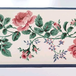 May include: Floral wallpaper border featuring pink roses, green leaves, and small blue flowers on a cream background. The design includes a dark blue border at the top and bottom, creating a classic, vintage aesthetic.