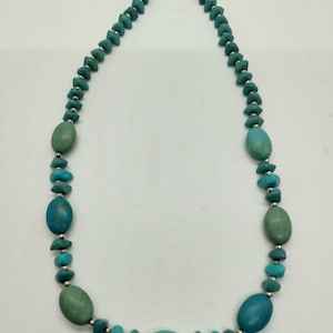 Op de afbeelding: Een turquoise ketting met een zilveren sluiting. De ketting heeft een verscheidenheid aan turquoise kralen in verschillende vormen en maten, waaronder ovale en onregelmatige vormen. De kralen zijn een mix van licht- en donker turquoise kleuren.