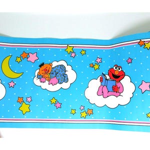 May include: Blue wallpaper border featuring Sesame Street characters. Ernie sleeps on a cloud, while Elmo reads a book. The border has a light blue background with white polka dots, pink and yellow stars, and a yellow crescent moon.