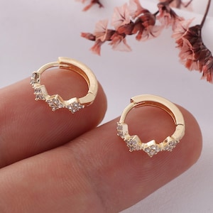 May include: A pair of gold hoop earrings with a row of small, clear cubic zirconia stones on each hoop.