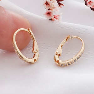 May include: A pair of gold hoop earrings with a row of small clear stones around the edge.