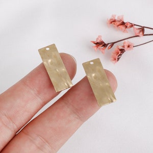 May include: Two gold-colored metal rectangular tags with a hammered texture and a hole at the top for hanging.
