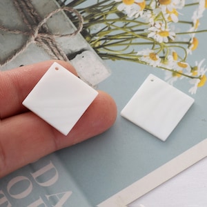 May include: Two white square-shaped acrylic blanks with a hole in the center. The blanks are on a white surface.