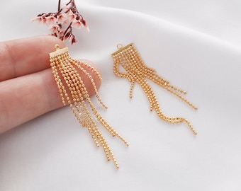 May include: Two gold-colored tassel earrings with a chain-like design. Each earring has a small rectangular piece at the top.