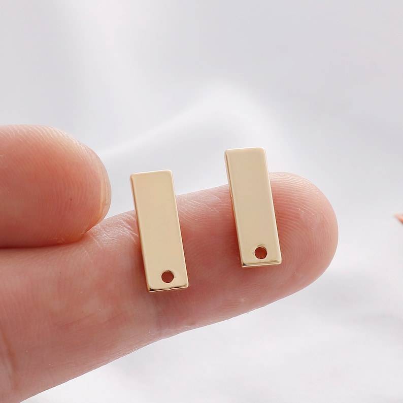 K&ouml;nnte beinhalten: Zwei goldfarbene, rechteckige Anh&auml;nger mit einem kleinen Loch unten. Die Anh&auml;nger sind glatt und gl&auml;nzend und reflektieren das Licht. Diese Schmuckzubeh&ouml;rteile sind ideal f&uuml;r die Herstellung personalisierter Halsketten, Armb&auml;nder oder Ohrringe.