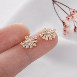 May include: A pair of gold-tone earring charms with a fan-shaped design featuring clear cubic zirconia stones.