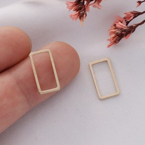 May include: Two gold-colored metal rectangle shapes, each with a hollow center. The shapes are small and are shown on a white surface.