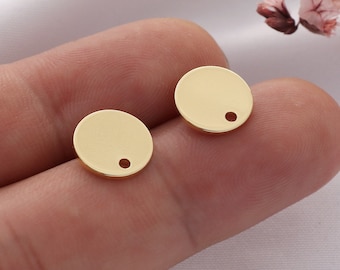 May include: Two gold-colored metal round disc charms with a small hole in the center. The charms are on a finger.