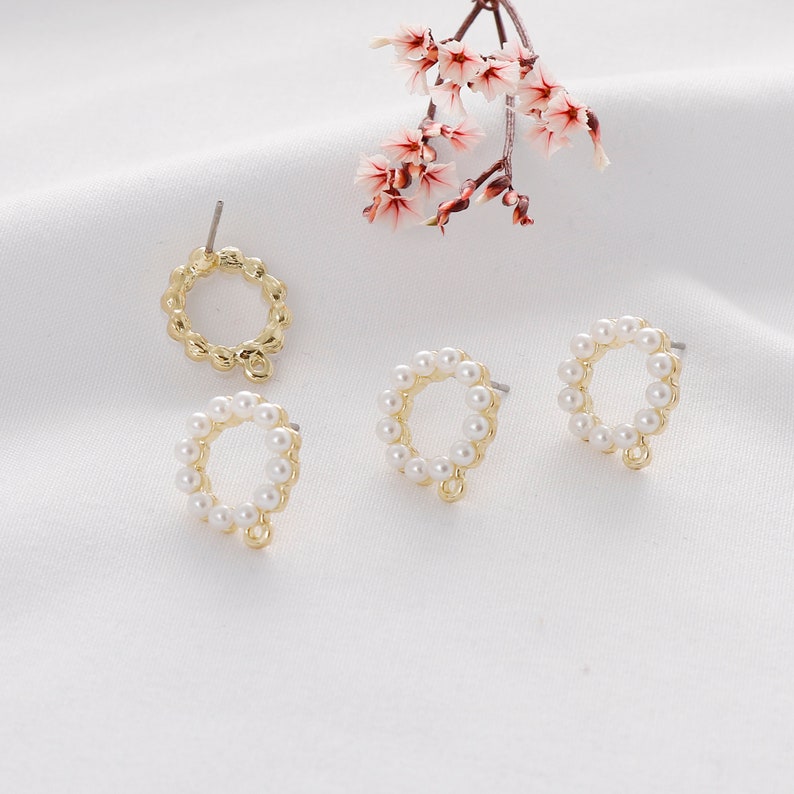 Puede incluir: Pendientes de metal dorado con un dise&ntilde;o circular. Cada pendiente presenta un anillo de peque&ntilde;as perlas blancas. Los pendientes tienen un cierre de poste y un peque&ntilde;o lazo en la parte inferior. Una ramita de flores rosas est&aacute; en el fondo.