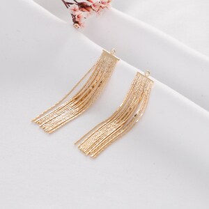 May include: A pair of gold dangle earrings with a chain tassel design. The earrings are made of metal and have a simple, elegant look.