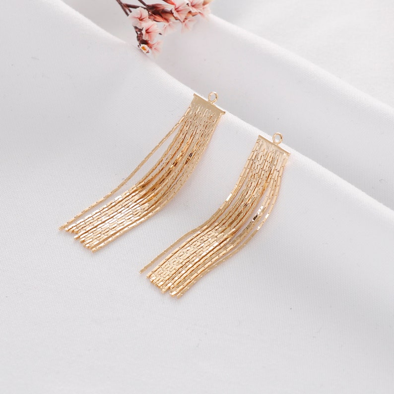 May include: A pair of gold dangle earrings with a chain tassel design. The earrings are made of metal and have a simple, elegant look.