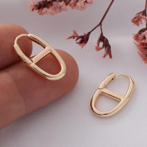 May include: A pair of gold hoop earrings with a unique oval shape and a smaller oval cutout in the center.
