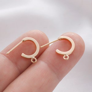 May include: Two gold-toned earring hoops with a jump ring at the bottom. The hoops are open and have a straight post.