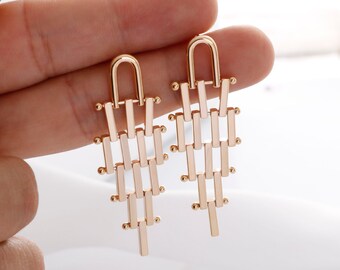 May include: A pair of gold-toned dangle earrings with a geometric design. The earrings are made of a series of interconnected bars that create a cascading effect.