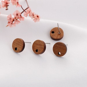 May include: Three round wooden earrings with a small hole in the center. The earrings are a light brown color and have a natural wood grain.
