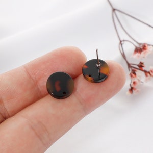 May include: Two round, brown and black, tortoise shell patterned earring blanks with a hole in the center. One earring blank has a silver post attached.