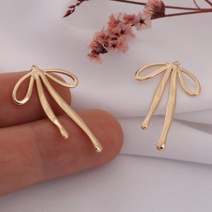 May include: Two gold-coloured metal bow-shaped earring charms.