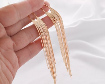 May include: A pair of gold dangle earrings with a fringe design. The earrings are long and have a delicate, feminine look.