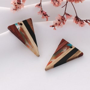 Peut inclure: Deux pendentifs triangulaires en bois avec un motif rayé noir, brun et blanc et un incrustation de résine colorée. Les pendentifs ont un trou en haut pour accrocher.