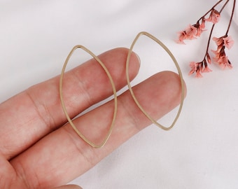 May include: A pair of gold-toned, open oval-shaped earrings. The earrings are made of thin metal and have a simple, minimalist design.