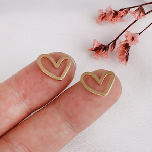 May include: Two gold-colored heart-shaped earrings with a hollow center. The earrings are small and delicate.