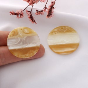 May include: Two round, cream and brown marbled resin embellishments with a hole in the top for hanging.