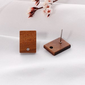 May include: A pair of wooden earrings with a square shape and a small hole in the center. The earrings are brown and have a natural wood grain.