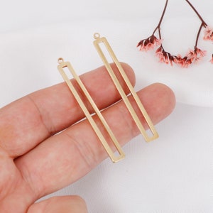 May include: Two gold-colored metal rectangular earring blanks with a loop at the top. The blanks are about 2 inches long.