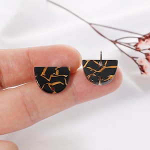 May include: A pair of black and gold half-circle earrings with a crackled effect. The earrings have a gold metallic finish and are made of resin.