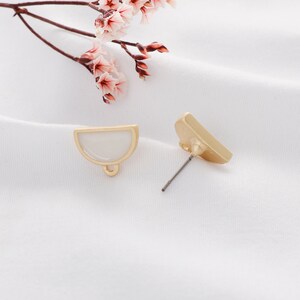 May include: A pair of gold-tone earrings with a white half-circle design. The earrings have a post back and a loop on the top.