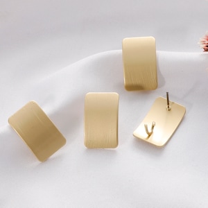May include: Four gold-coloured rectangular earrings with a brushed finish. The earrings are on a white surface.