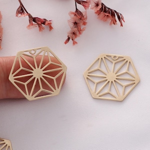 May include: Two gold-toned metal hexagon-shaped charms with a geometric starburst design. The charms have a small hole at the top for attaching to jewelry or other crafts.