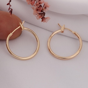 May include: A pair of gold hoop earrings with a simple, classic design. The earrings are made of a smooth, polished metal and have a hinged closure.